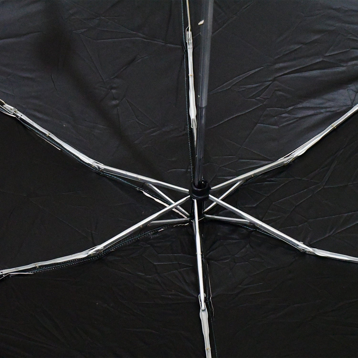 The interior of a black umbrella reveals its silver metal spokes and central mechanism.
